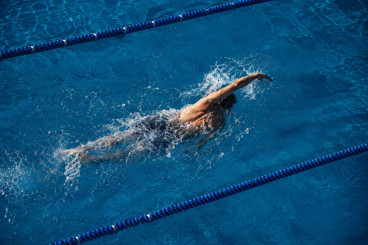 An adult swimmer training in a sunlit blue pool